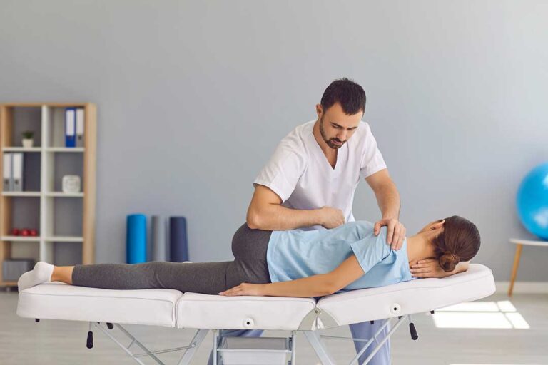 A chiropractor gently examines a patient’s upright spine in a bright clinic setting.