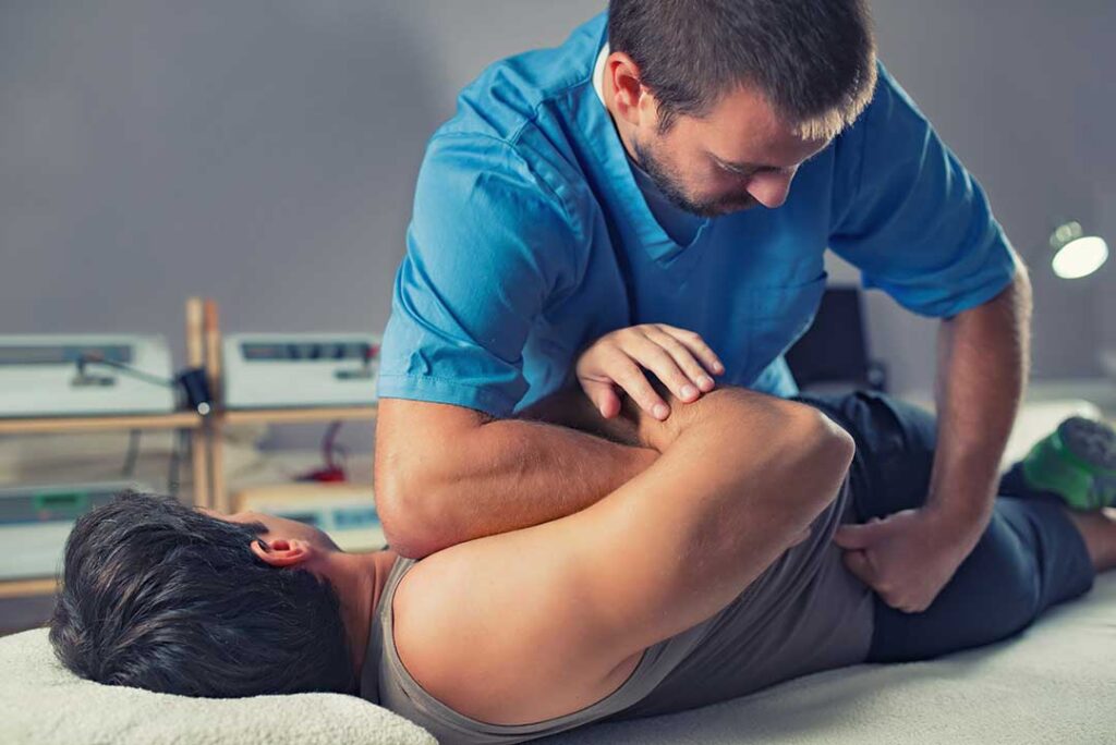 An adult sitting on a couch using a heating pad on their lower back.